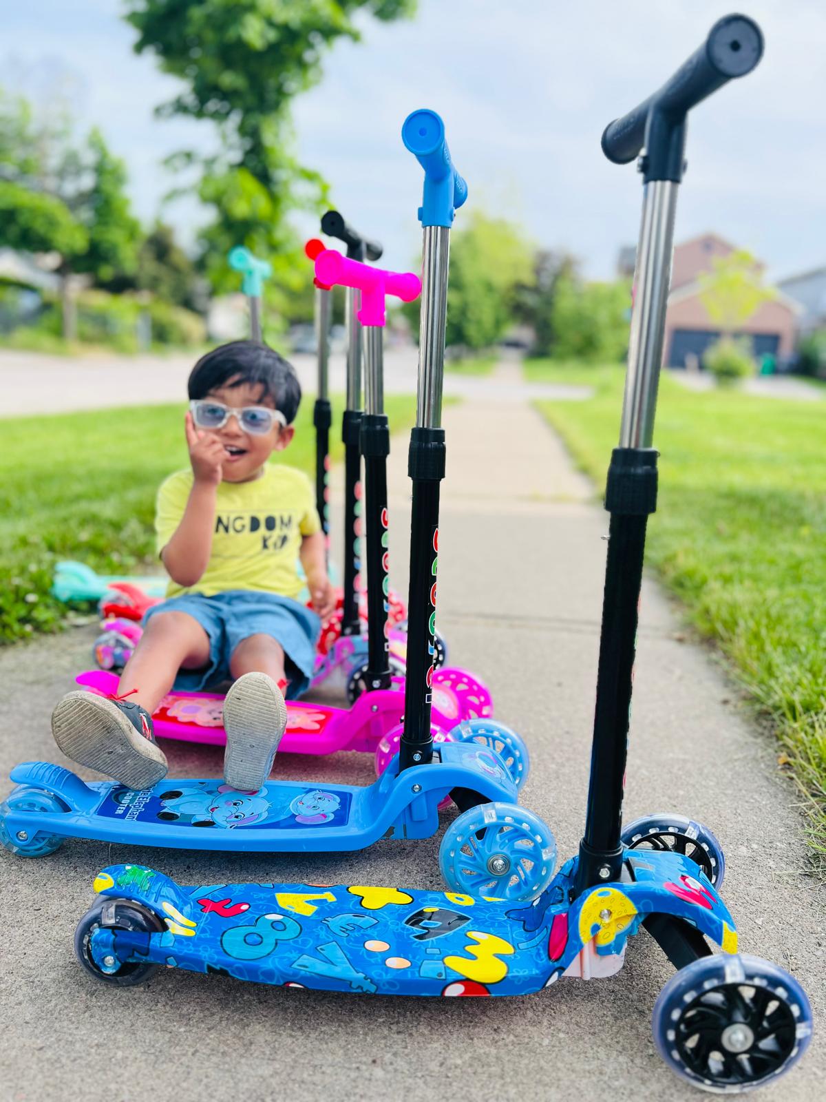 "A group of colorful 3-wheel scooters with a young boy sitting on one, ready for adventure. Contact Giant Galaxi for more information on our fun and safe scooters for kids."