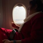 A passenger in a red outfit and white scarf sits by an airplane window, symbolizing the "Canada wide" reach of Giant Galaxi.